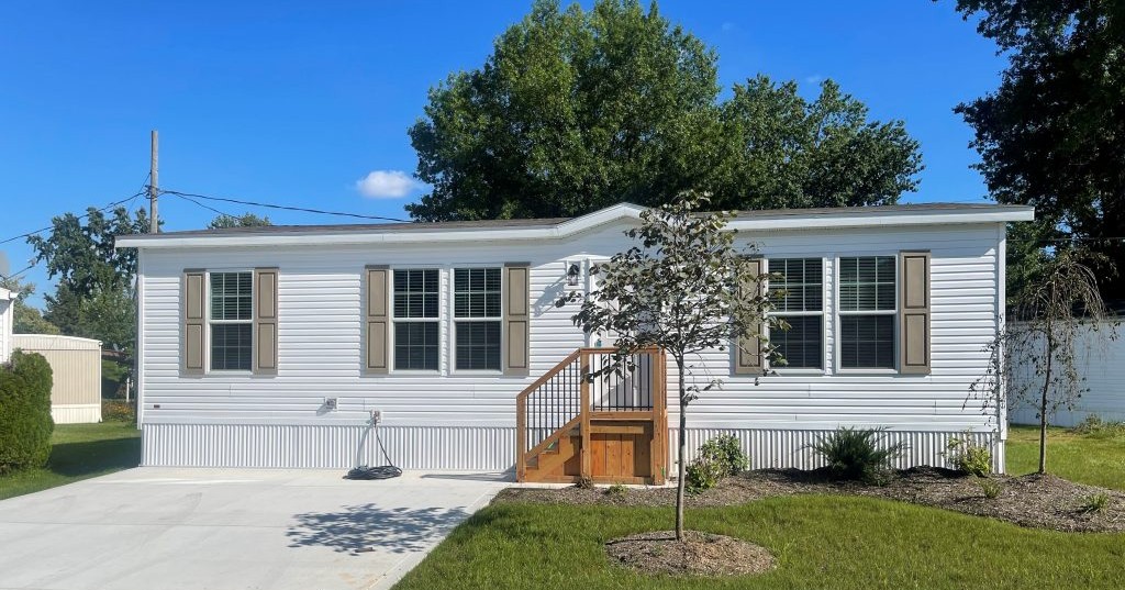 Single-story manufactured home exterior with white siding, front steps, and paved driveway in Columbia Park